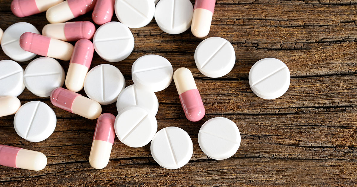 A collection of pills and pill capsules lying on a wooden surface.